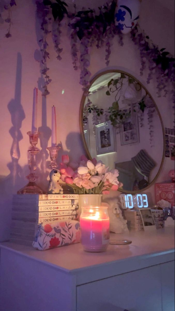 a table topped with a vase filled with flowers next to a mirror and candles on top of it