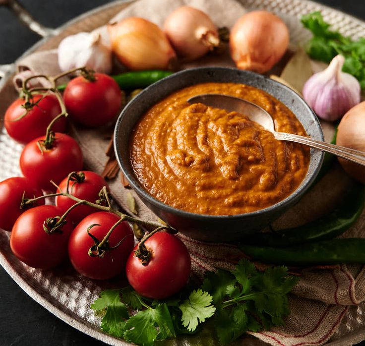 a bowl of tomato hummus next to some tomatoes and garlic on a platter