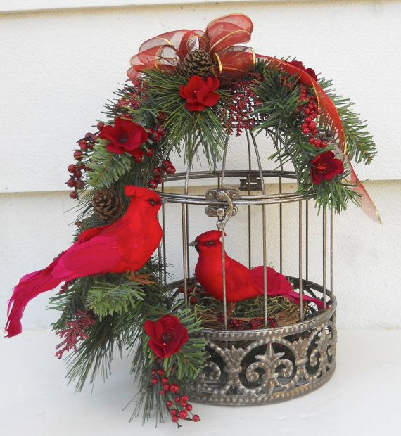 two red birds sitting in a birdcage decorated with pine cones, holly and poinsettis