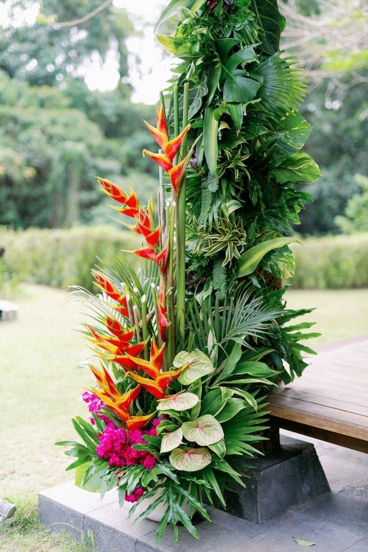 an arrangement of tropical plants and flowers on a bench in front of a park area