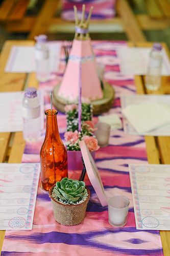 a table topped with pink and purple place mats covered in paper plates filled with succulents