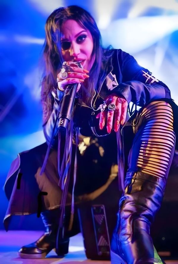 a woman in black leather boots on stage with her hand over her mouth while holding a microphone