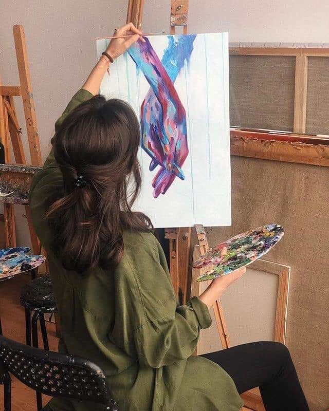 a woman sitting in front of an easel painting