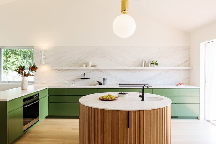 a large kitchen with green cabinets and marble counter tops, along with an island in the middle