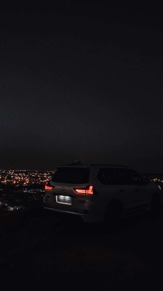 the back end of a car parked on top of a hill at night with city lights in the background