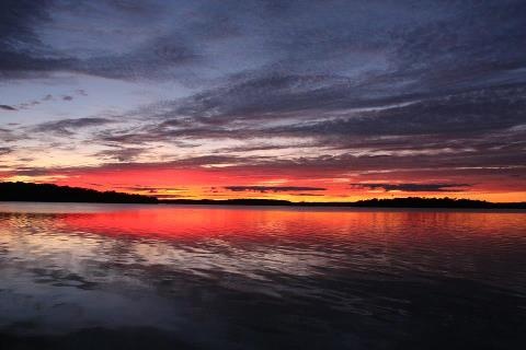 the sun is setting over the water and clouds are reflected in the water as it sets