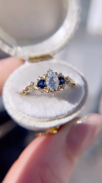 a person holding an open ring box with two blue stones in it's center