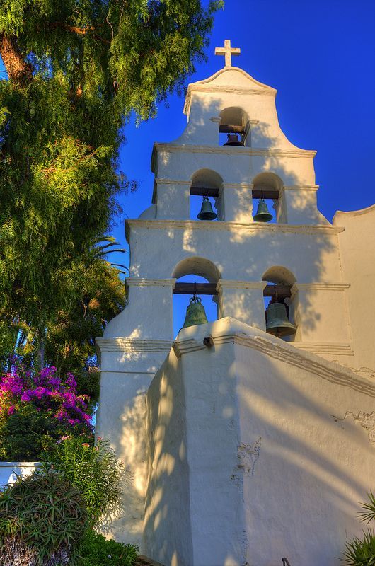 an old church with bells on the side and trees in the foreground against a blue sky