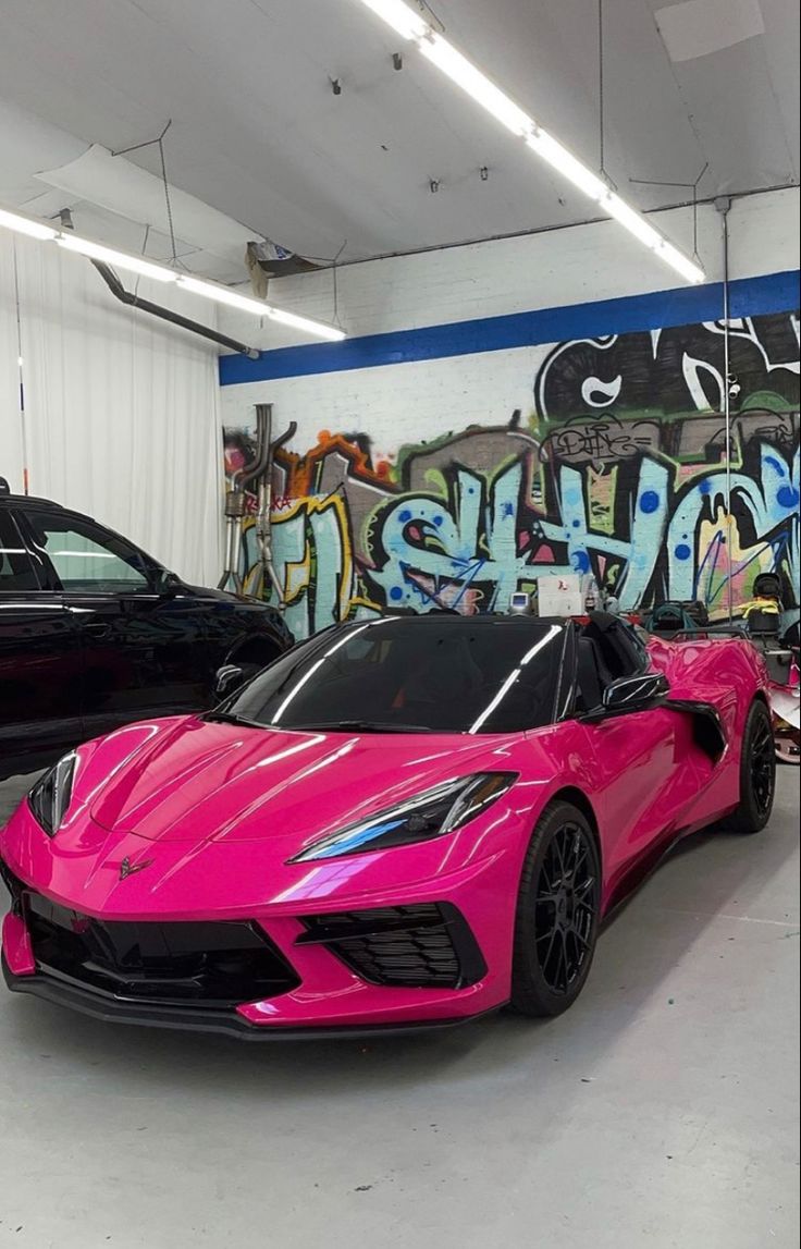 two pink sports cars parked next to each other in a garage with graffiti on the wall