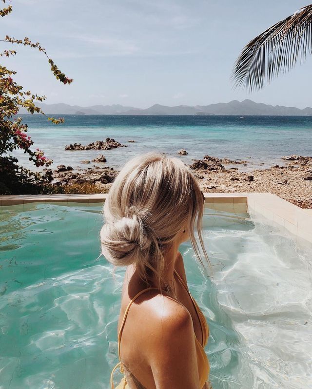 a woman in a yellow swimsuit is looking out at the ocean from an outdoor jacuzzi