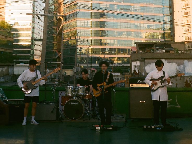 three young men are playing instruments on the roof of a building in front of skyscrapers