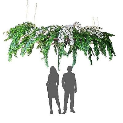 two people standing under a green plant hanging from the ceiling with white flowers and greenery