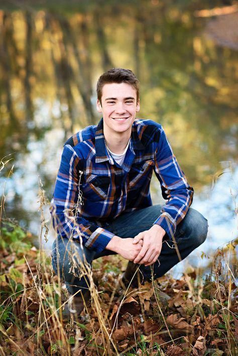 a young man sitting on the ground in front of a pond smiling at the camera