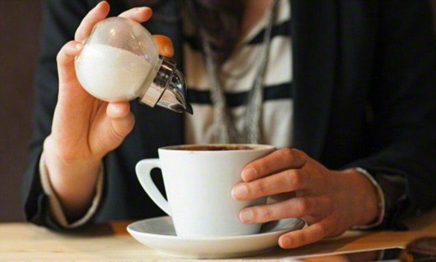 a woman is pouring something into a cup with a spoon on the table in front of her