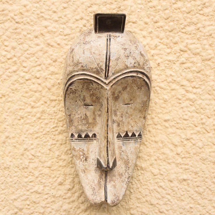 an old mask is mounted on the side of a stucco - colored wall with black accents