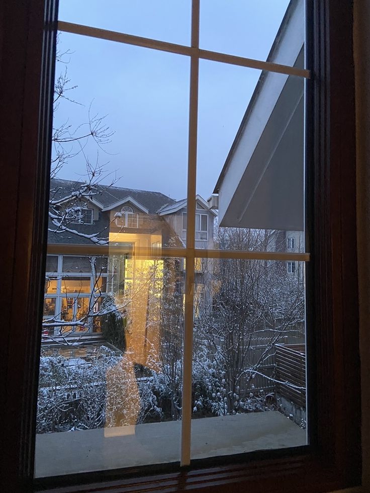 a window with a view of houses and trees in the snow from inside an apartment building