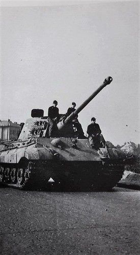 men sitting on top of an old tank in the middle of road with other tanks behind them