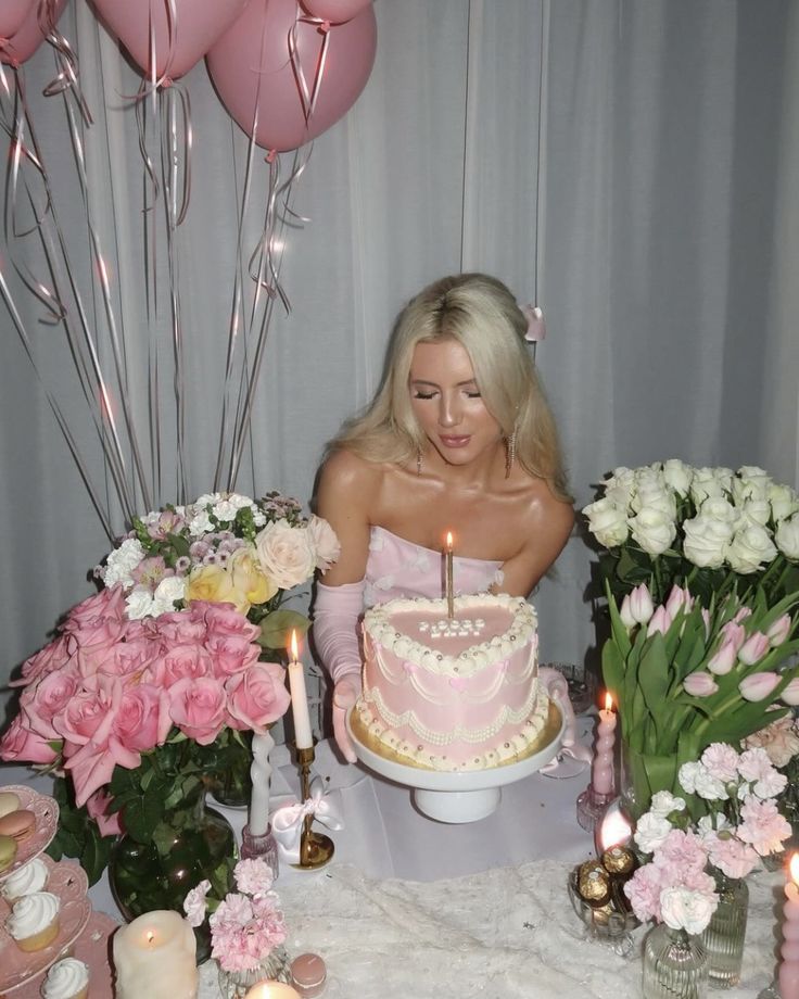 a woman sitting in front of a cake with candles on it and flowers around her