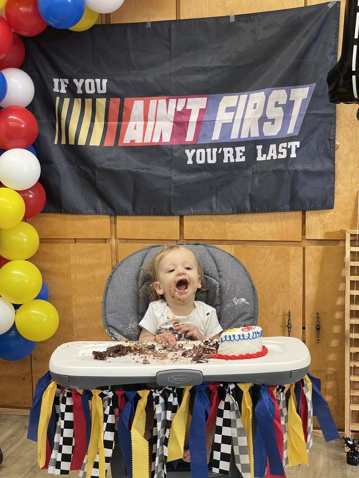 a baby is sitting in a highchair with a cake and balloons around him