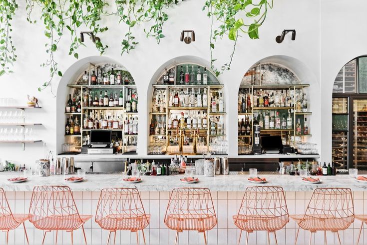 the bar is decorated with greenery and pink chairs, which are lined up against the wall