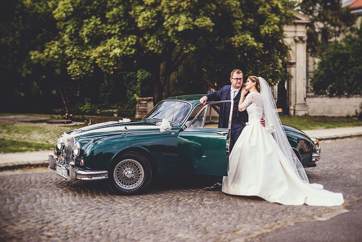 a bride and groom standing in front of a green vintage car on a cobblestone street