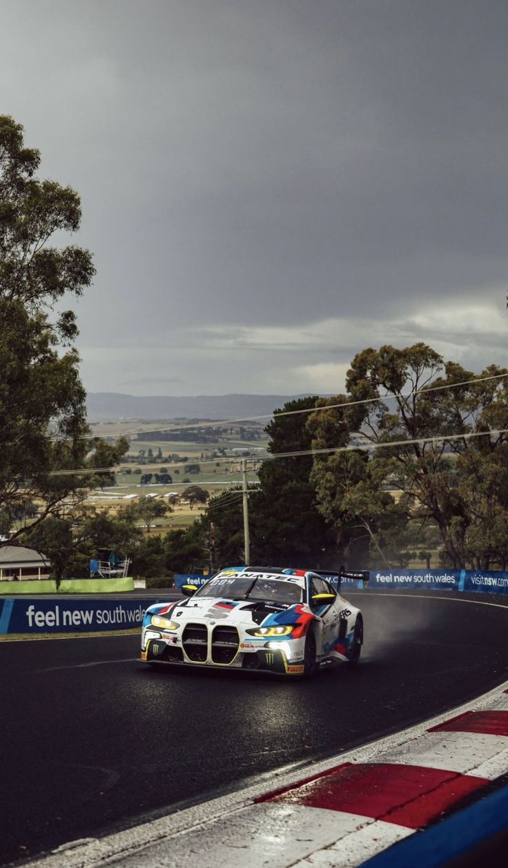 a car driving down a race track with trees in the background and dark clouds overhead