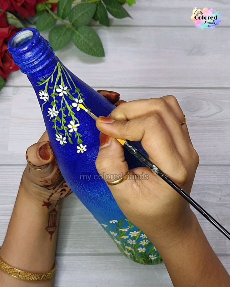 a woman is painting a blue vase with flowers on it