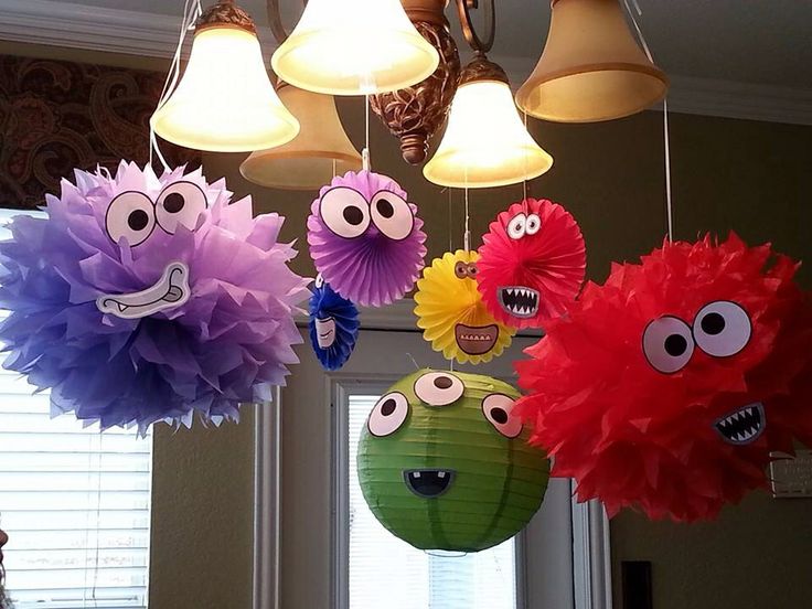 some paper decorations hanging from the ceiling with eyes and mouths on them in front of a window