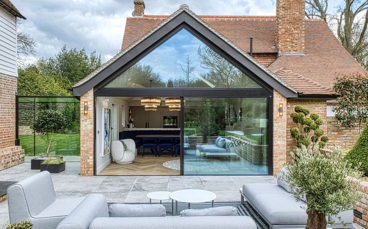 an outdoor living area with couches and tables in front of a brick building that has glass doors leading into the back yard