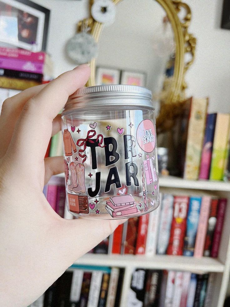 a person holding up a jar with writing on it in front of a bookshelf