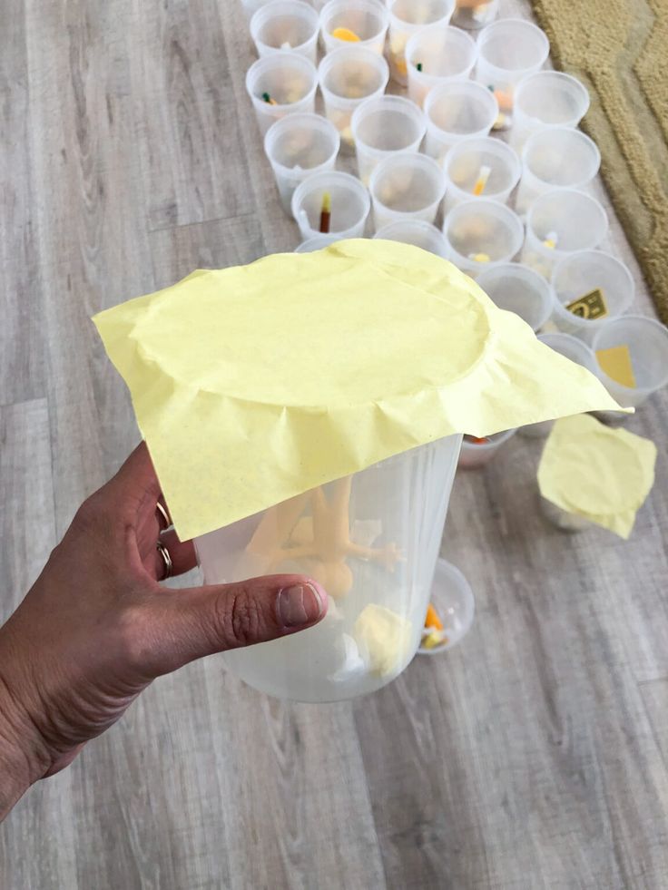 a hand holding a yellow piece of paper over a container filled with plastic cups on a wooden floor