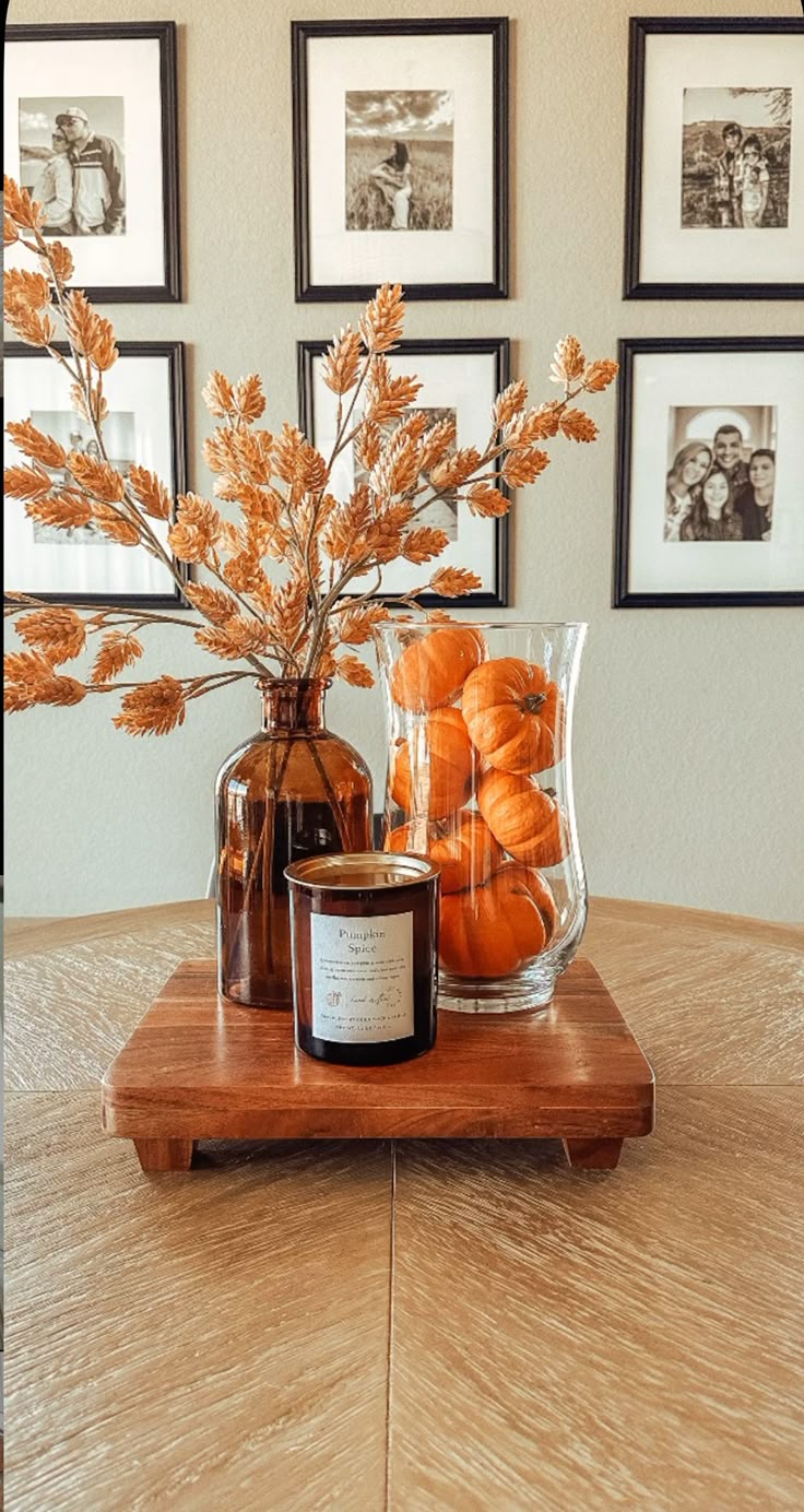 an arrangement of pumpkins in a glass vase on a wooden table with framed pictures