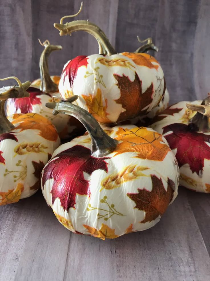 four pumpkins with leaves painted on them are sitting on a table together in front of a wooden background