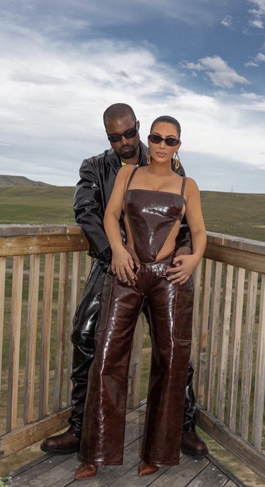 a man and woman in leather outfits posing for a photo on a wooden deck with mountains in the background