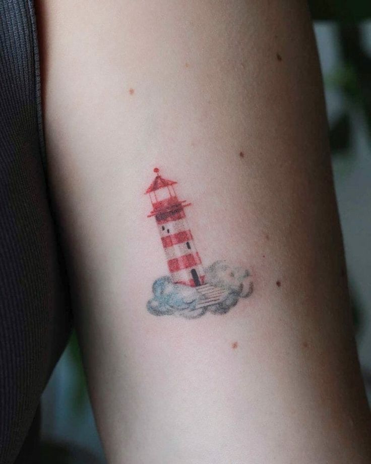 a small red and white lighthouse tattoo on the right side of the left arm with clouds around it