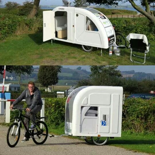 there is a man riding a bike next to a small trailer that looks like a camper