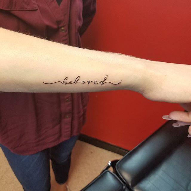 a woman with a tattoo on her arm that says, beloved in cursive writing