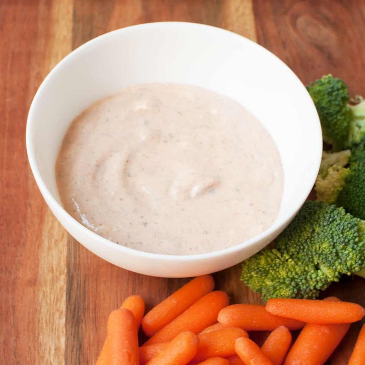 some carrots and broccoli on a cutting board next to a bowl of dip