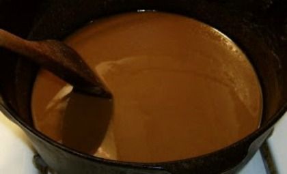 a wooden spoon in a pot filled with brown liquid on top of a white table