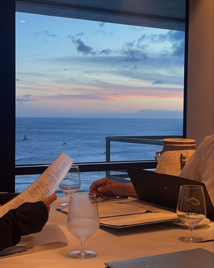 two people are sitting at a table with wine glasses and papers in front of them