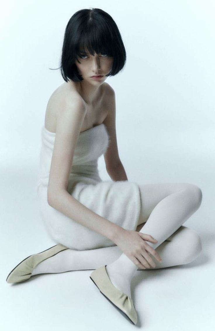 a woman sitting on the ground with her legs crossed, wearing white clothing and high heels