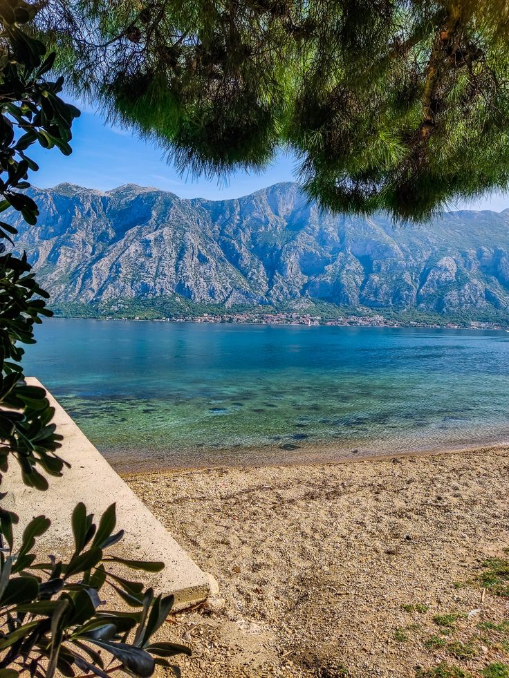 a beach with mountains in the background and clear blue water on one side that is surrounded by trees