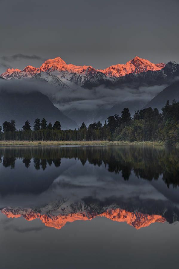 the mountains are covered in clouds and reflecting in the still water at sunset or dawn