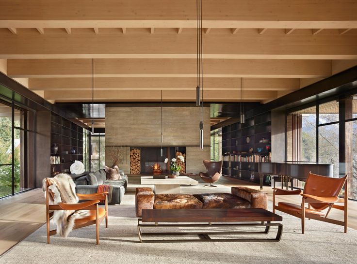 a living room filled with lots of furniture next to tall glass windows on the wall