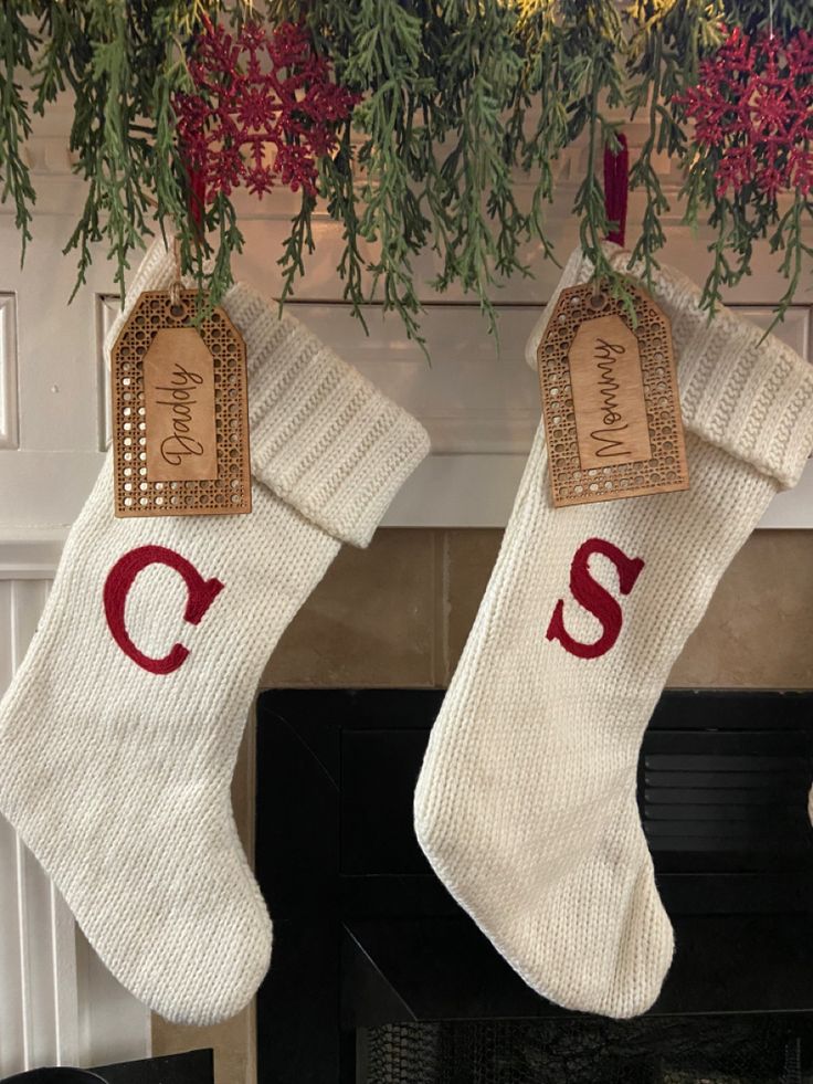 two stockings hanging from a mantel decorated with greenery