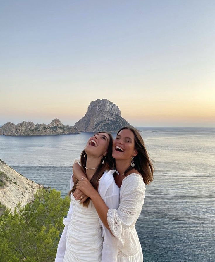 two women standing next to each other near the ocean