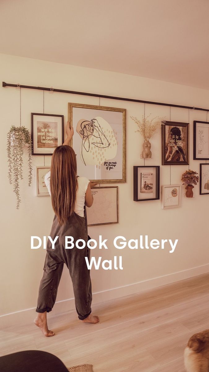 a woman standing in front of a wall with pictures on it and the words diy book gallery wall above her