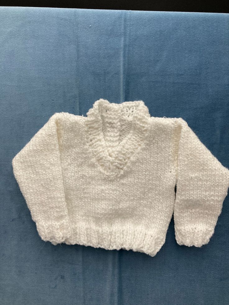 a white knitted sweater laying on top of a blue blanket