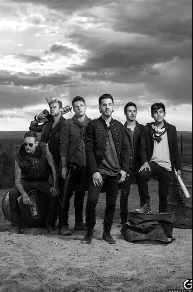 a group of men standing next to each other on top of a dirt field under a cloudy sky