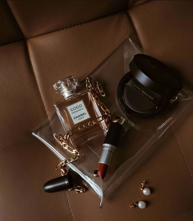 an open bottle of perfume sitting on top of a brown leather couch next to a black object